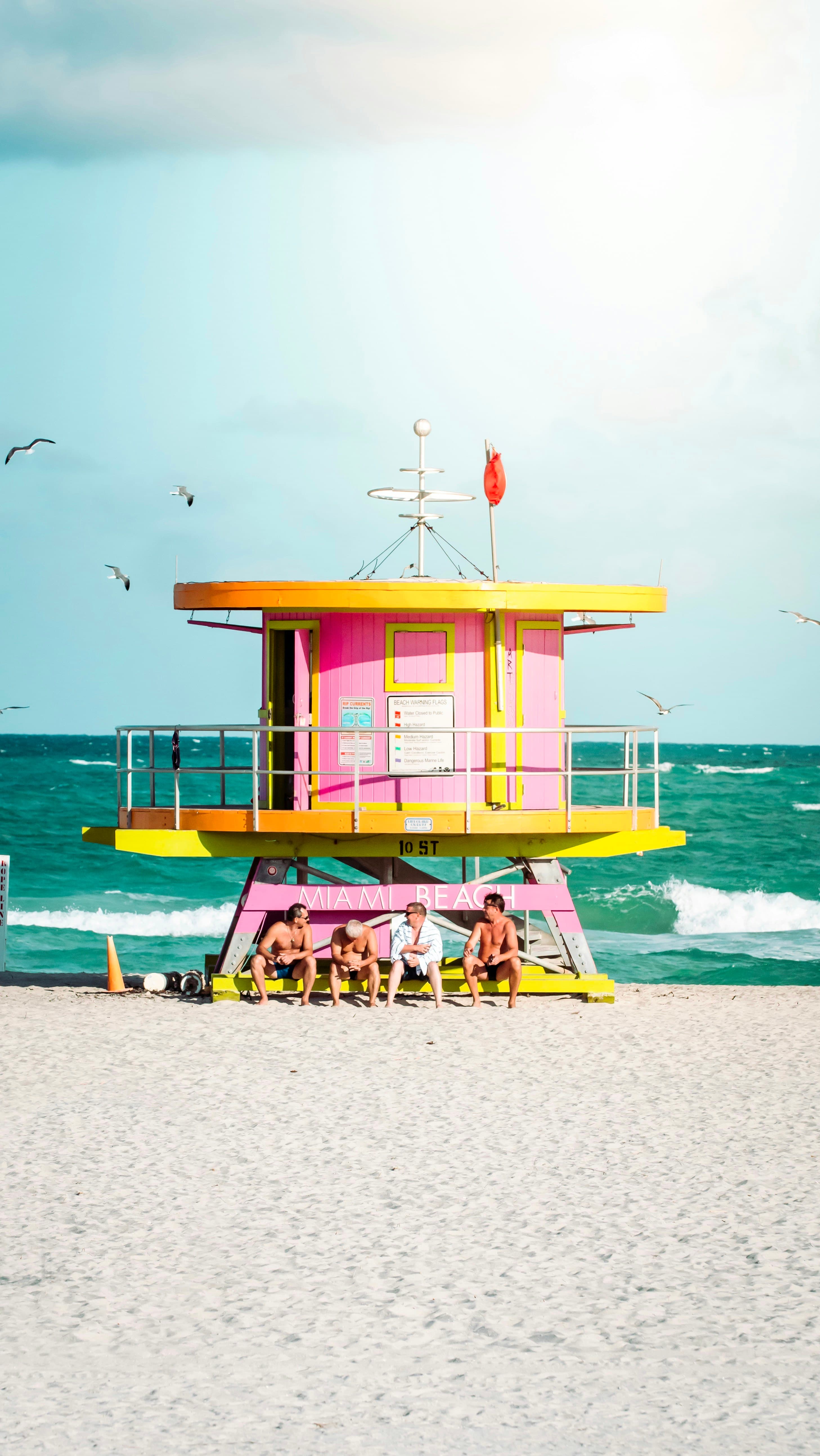 Friends sitting under a pink and yellow lifeguard tower on Miami Beach